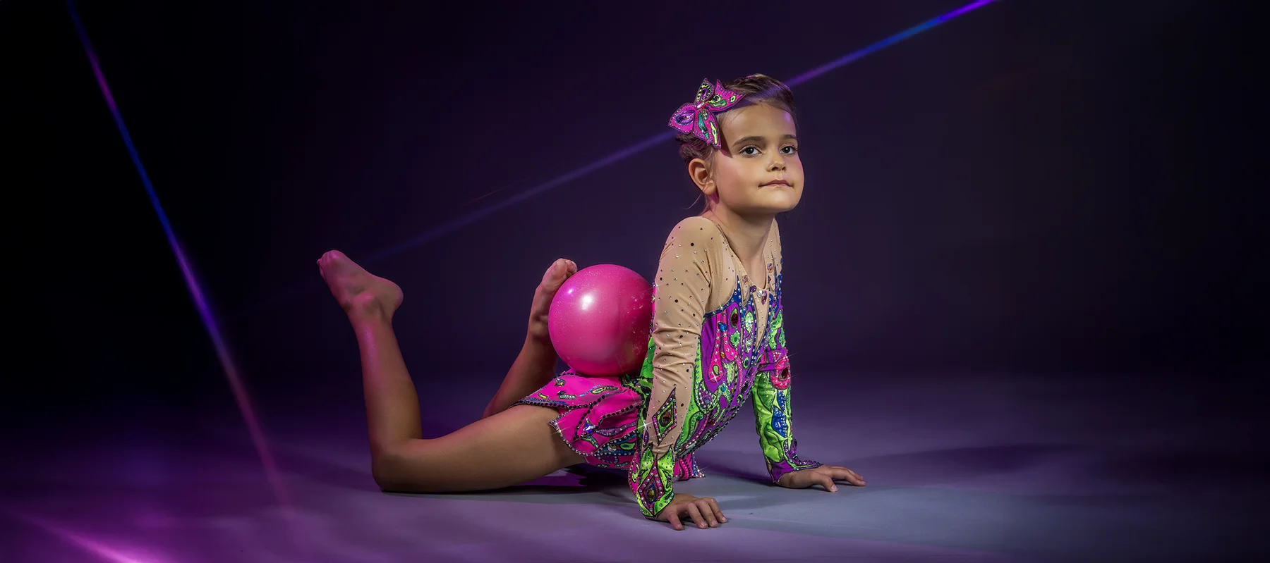 Rhythmic gymnast posing with ball in purple light