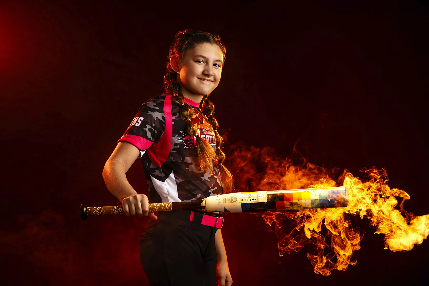 Softball girl holding a flaming bat in studio portrait