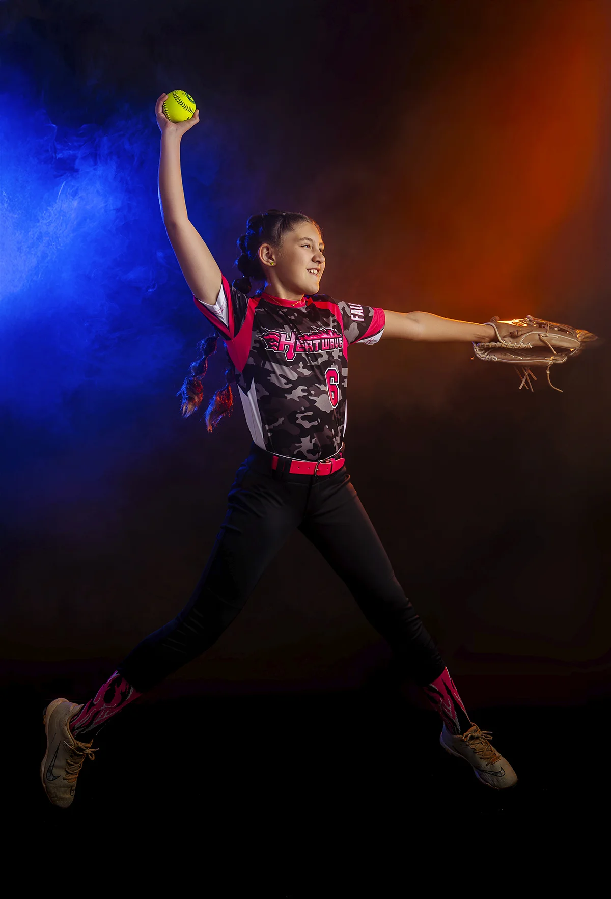 Softball girl pitching in mid-air with dramatic smoke background
