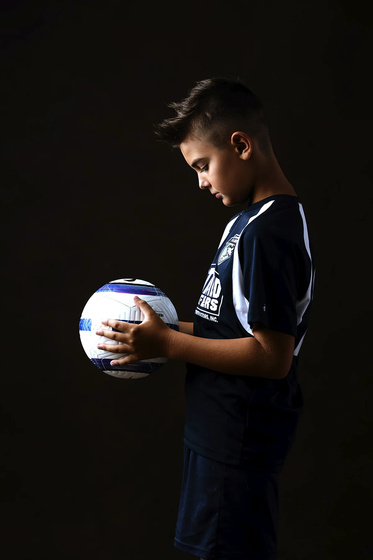 Soccer player holding ball in profile, moody dark background