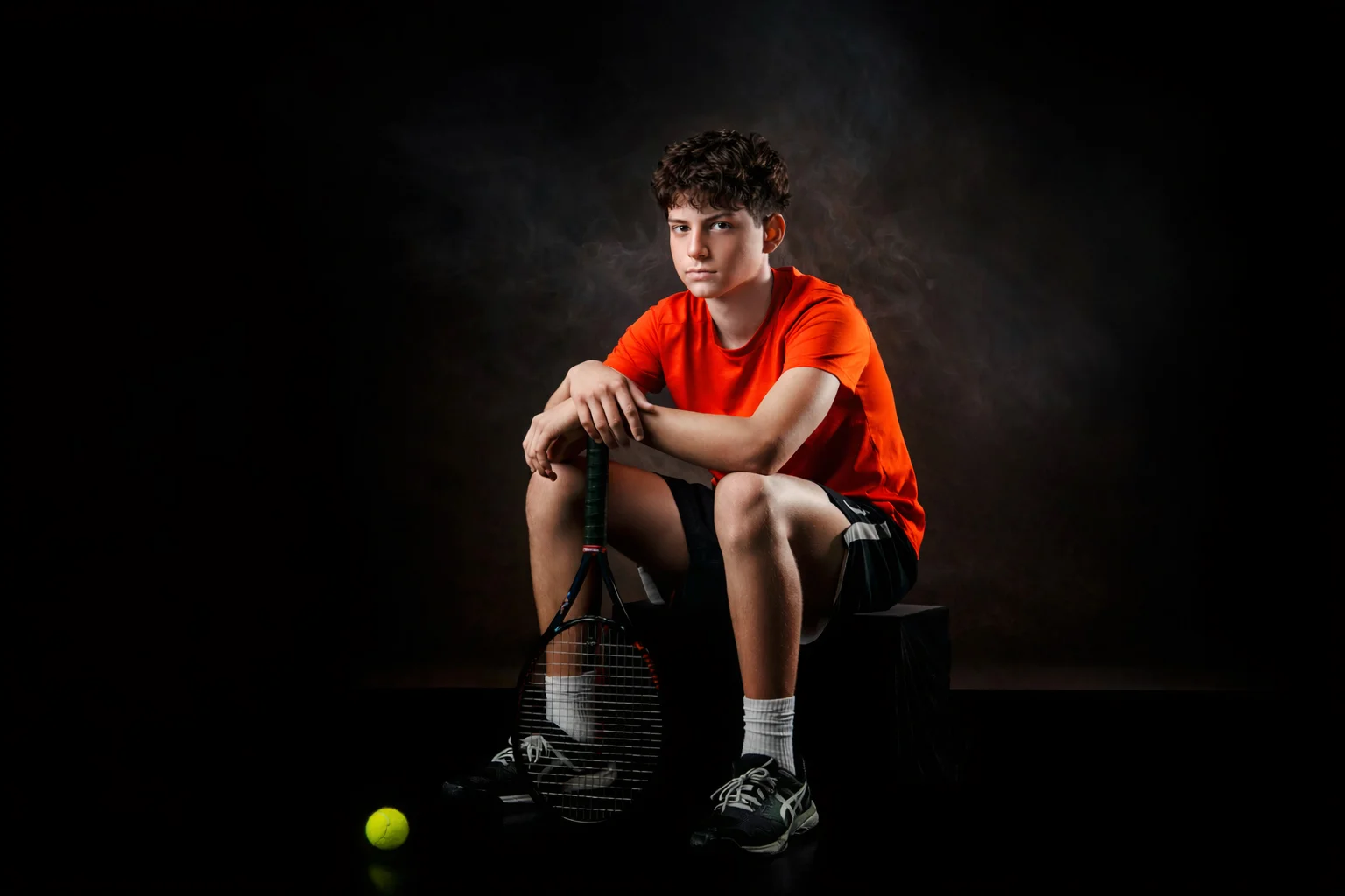 Tennis player seated with racket in dramatic studio lighting