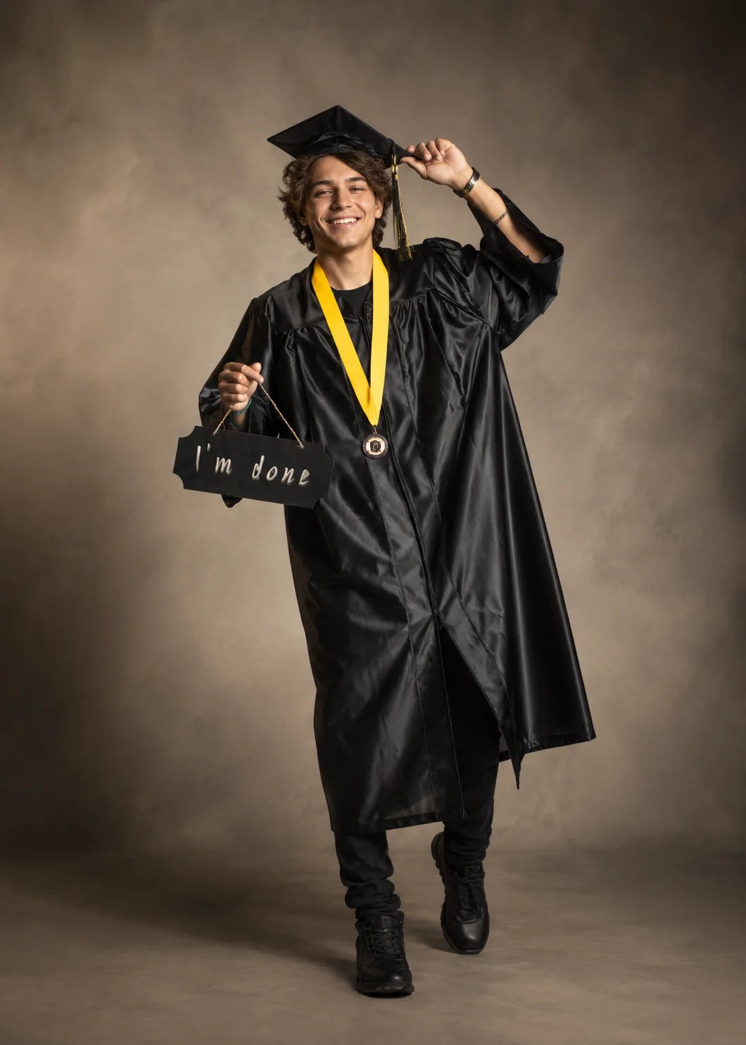 Smiling senior in cap and gown holding an "I'm done" sign, full-length studio portrait