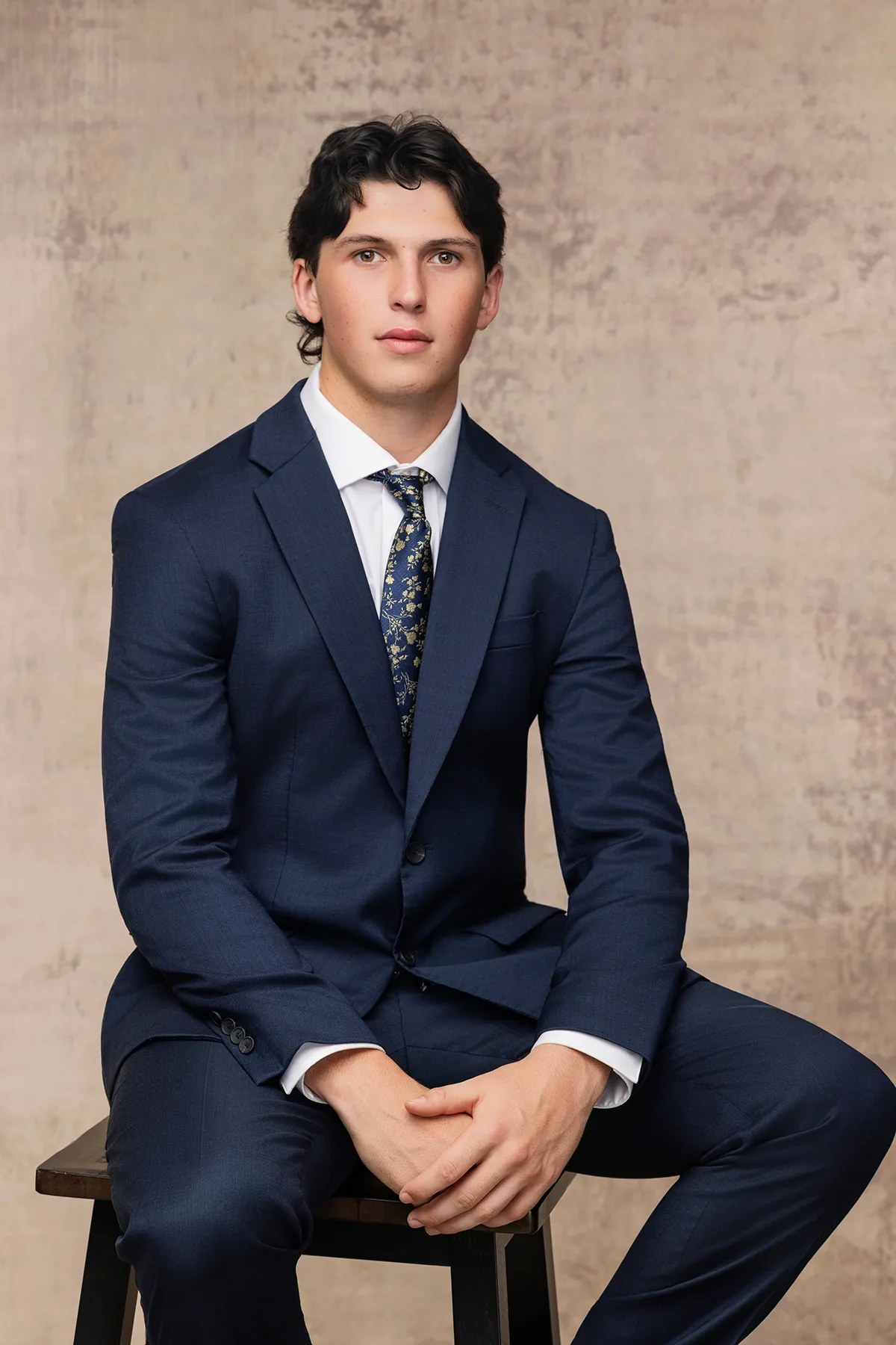 Senior in a navy suit and patterned tie, seated for a classic studio portrait