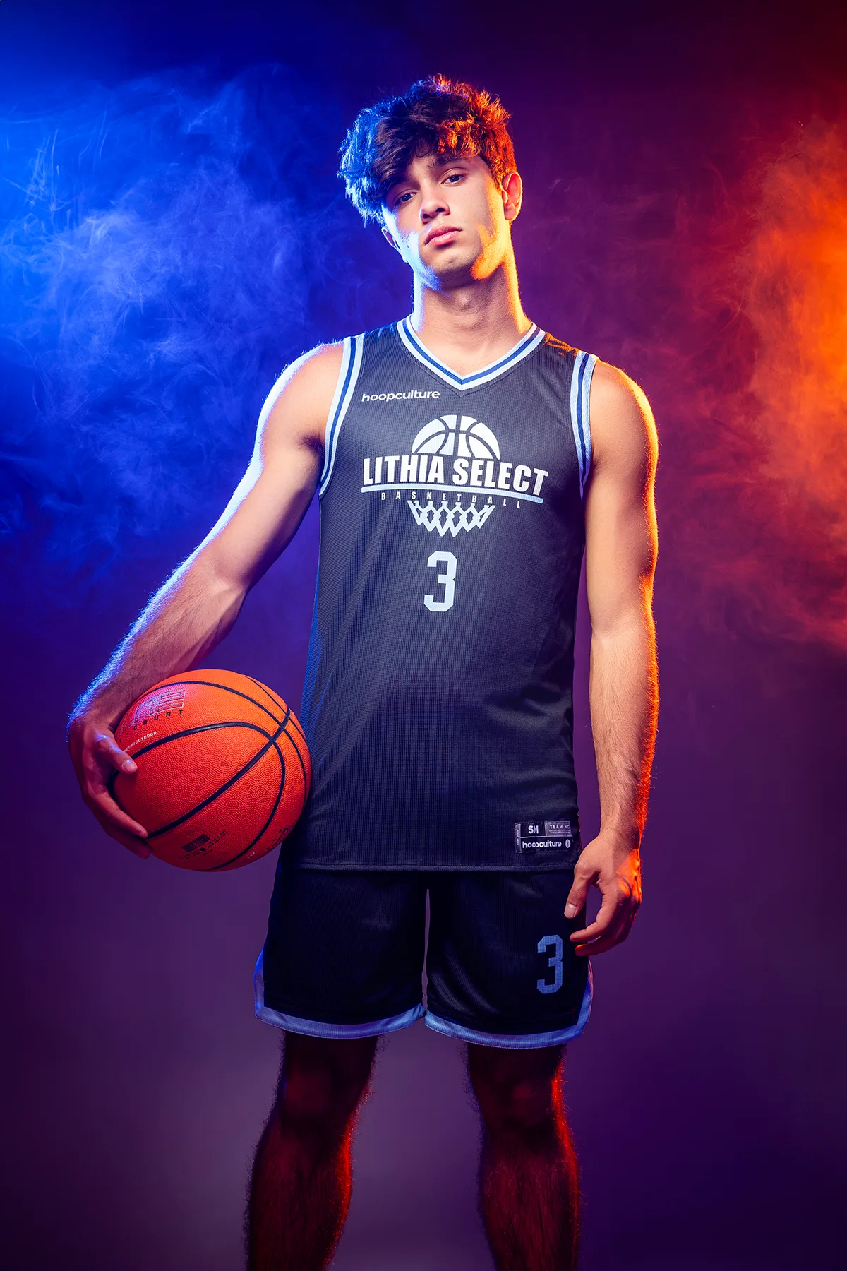Senior in a basketball jersey holding a ball, lit with blue and red studio gels