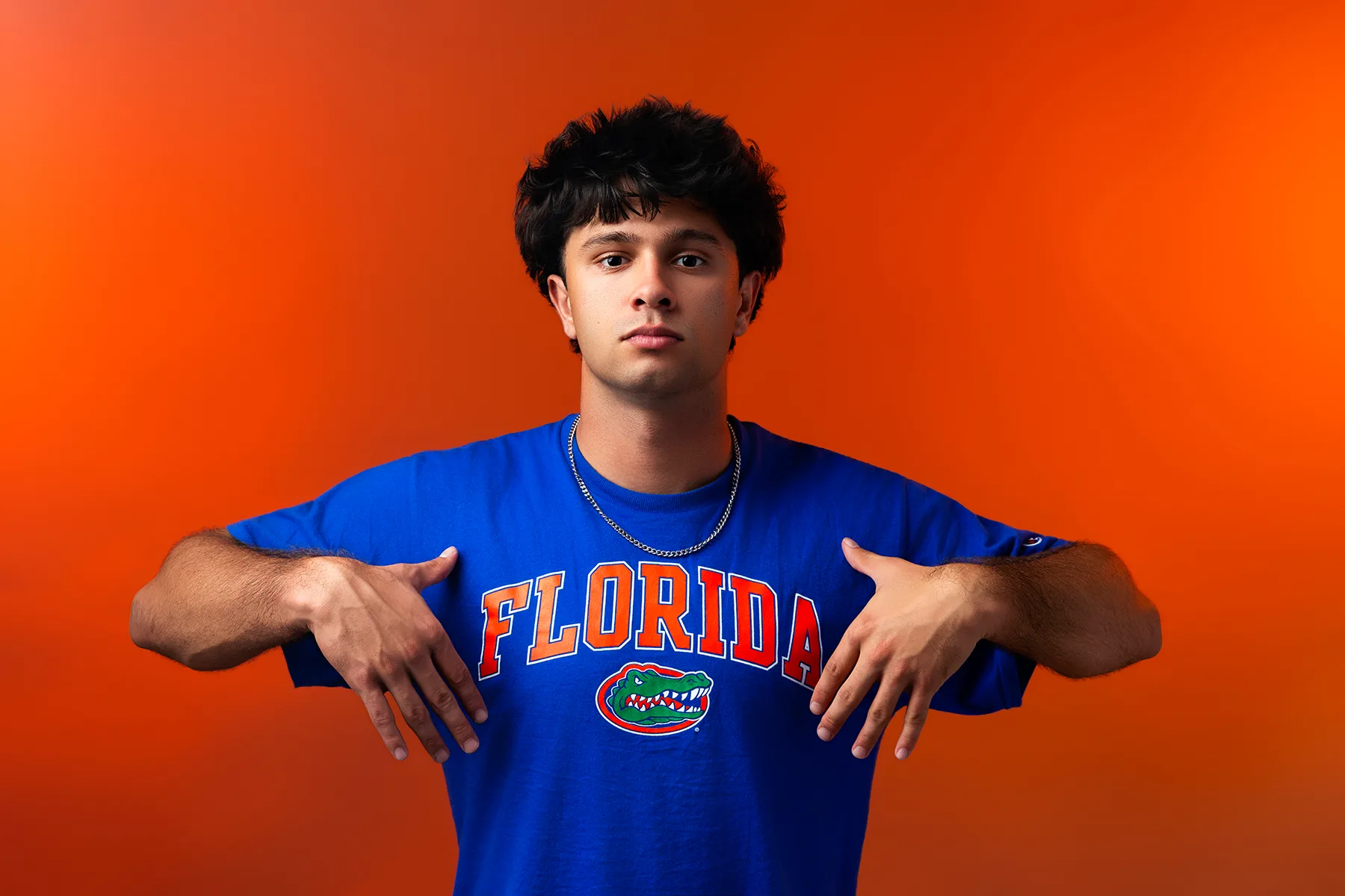 Senior pointing to his University of Florida tee against a bright orange backdrop