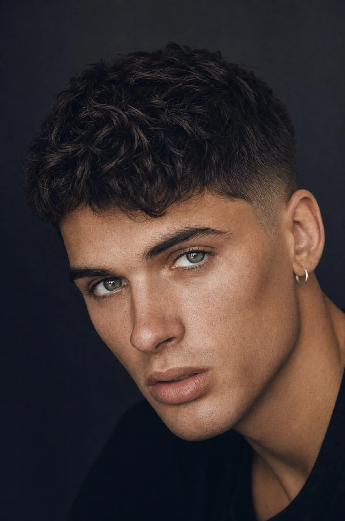 Close-up portrait showing styled hair and clear skin against a dark background